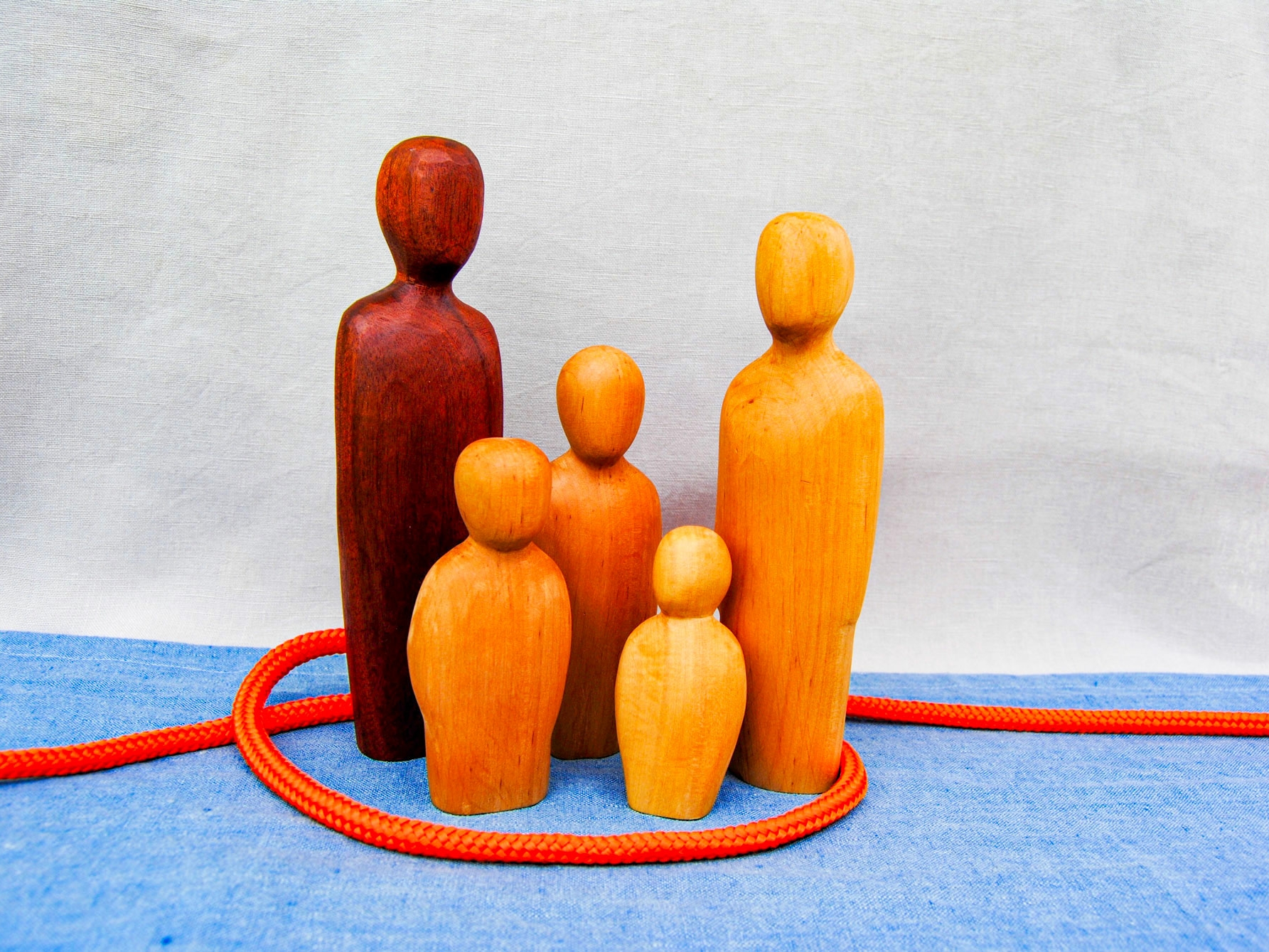 Es ist eine Familie mit drei Kindern dargestellt mit Holzfiguren. die von einem roten Band zu ihren Füßen umschlungen sind.