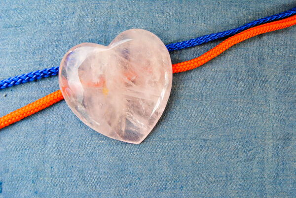 ein Herz aus Rosenquarz, glänzend geschliffen liegt auf zwei Schnüren - orange und blau - eine Paar-Timeline.
