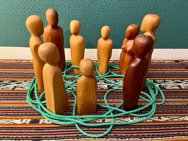 kollegiales Netzwerk Zu sehen sind 9 verschiedene Holzfiguren, die in einem Kreis stehen und auf dem Boden sind sie untereinander vielfältig verbunden durch grüne Schnüre.